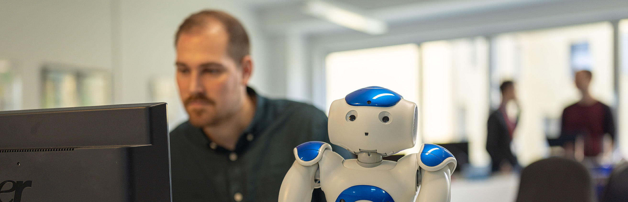 Student am PC mit humanoidem Roboter im Master-Studiengang Informatik